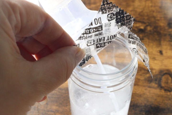手で個包装から取り出した錠剤型クリーナーを水が入った容器に入れている