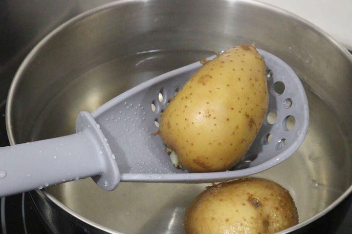 鍋で茹でているジャガイモをグレーの多機能ざるスプーンですくう。
