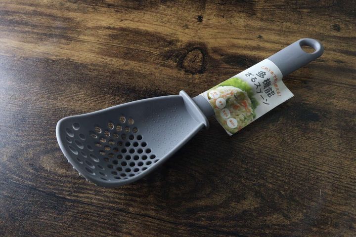 木目調のテーブルに斜めに置かれたグレーの多機能ざるスプーン。パッケージ付き。