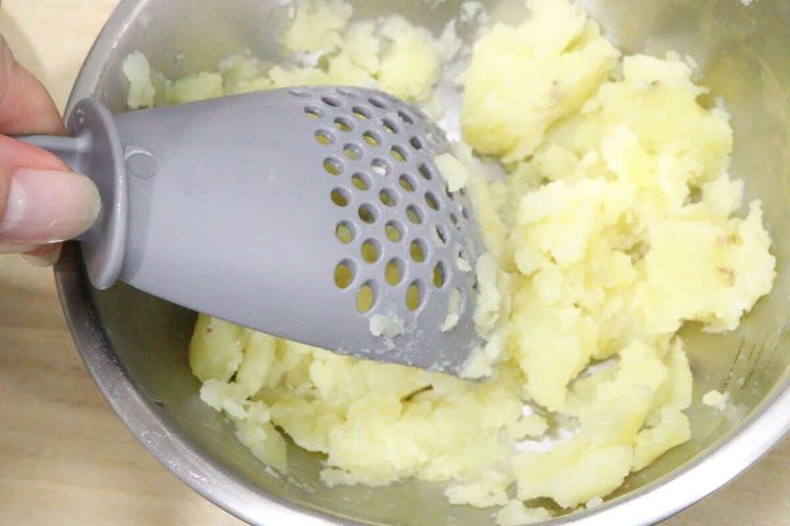ボウル内の茹でジャガイモを多機能ざるスプーンで押し潰している。