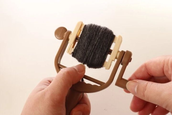 ボンボン＆タッセルメーカーにグレーの毛糸を巻き付けている両手