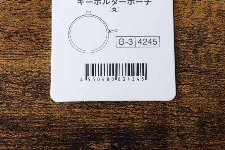 白い商品タグに記載された「キーホルダーポーチ（丸）」の文字とバーコードのクローズアップ