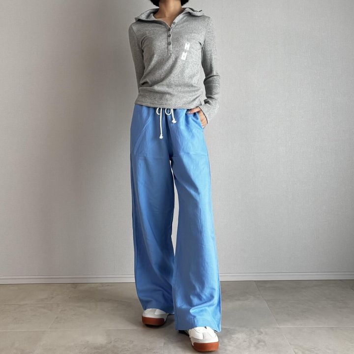 ブルーのリネンパンツとグレーの長袖トップスを着用した女性