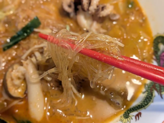 箸でつまむイイダコとあさりの５種野菜のチゲ鍋の春雨