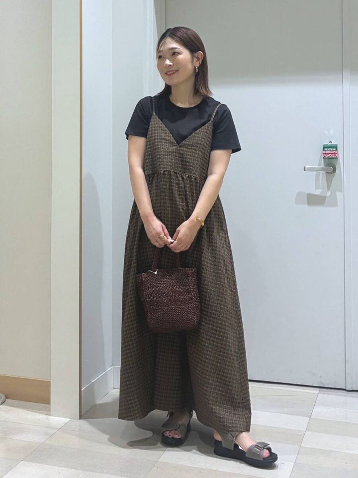 黒Tシャツにチェック柄キャミワンピを重ね着した女性