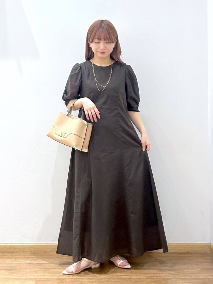 黒いパフスリーブワンピを着てベージュのバッグを持つ女性
