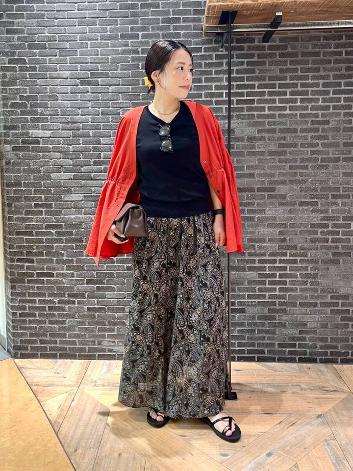 黒Tシャツにペイズリー柄スカート、赤いカーデの女性