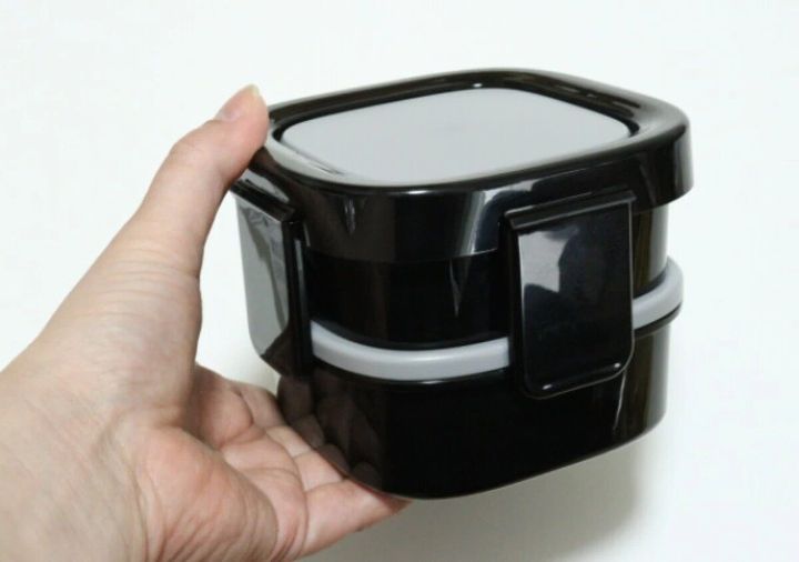 黒い2段式弁当箱を片手で持ち、サイズ感を示している