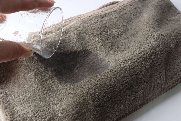 グラスから茶色のヘアドライタオルに水を垂らして吸水性を検証