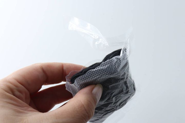 女性の手が個包装された黒いショート丈ソックスの封を開けている様子