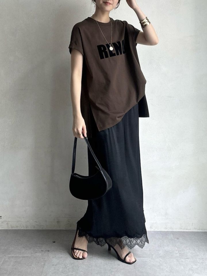 ブラウンロゴTと裾レース黒ロングスカートを着用しバッグを持つ女性
