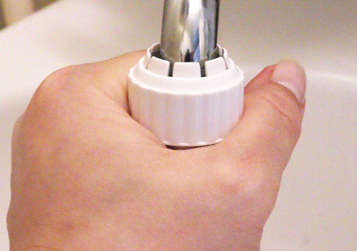 女性の手がセリアのキッチンシャワーを蛇口に取り付けている様子