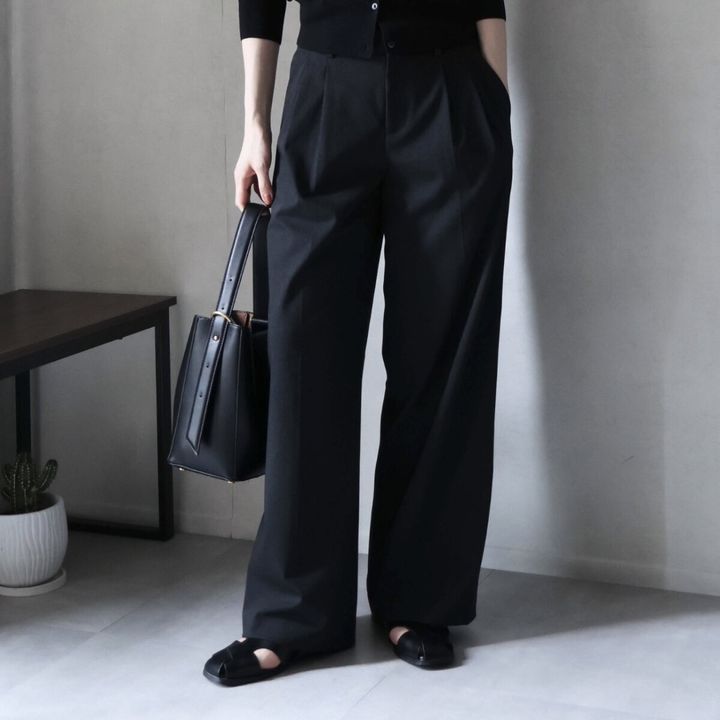 黒いワイドパンツと黒いカーディガンを着用し、バッグを持つ女性の全身