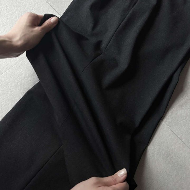 黒いパンツの生地を両手で引っ張り、伸縮性を確認している様子