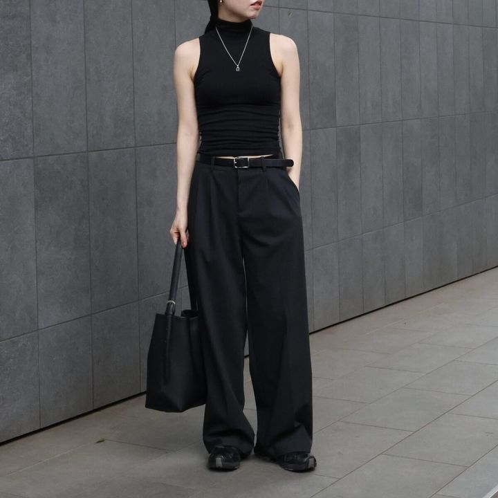黒いノースリーブとワイドパンツを着用し、バッグを持つ女性の全身