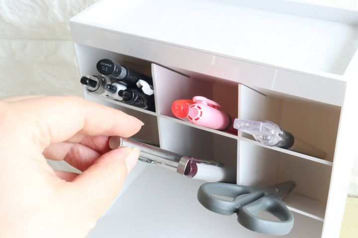 白い収納ケースの仕切りにペンやハサミを収納する女性の手元