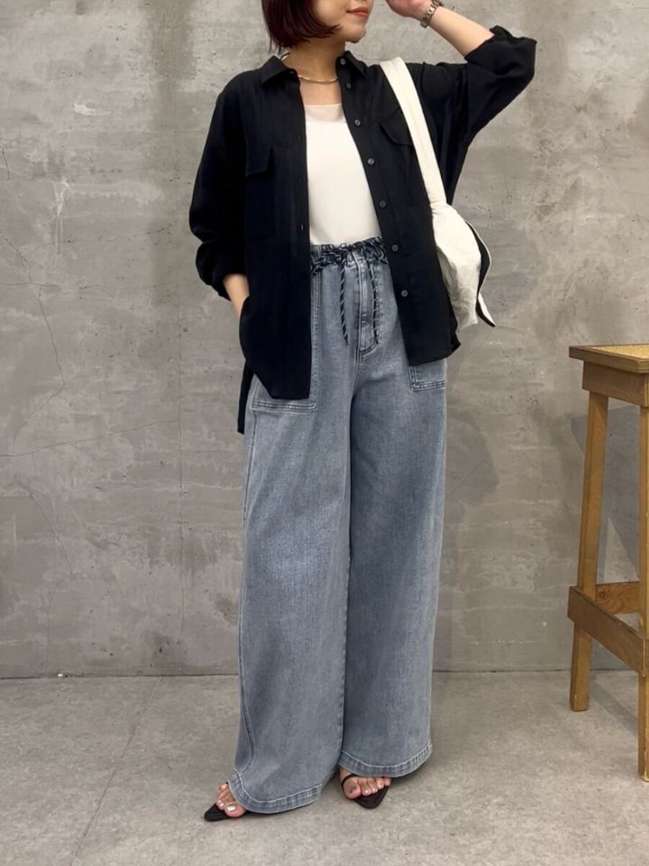 黒いシアーシャツとワイドデニムを着た女性が白いバッグを肩にかけている