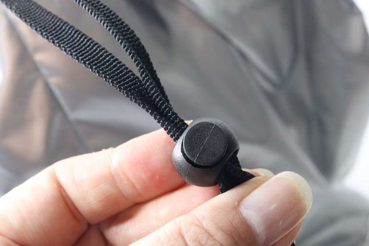 ナップサックの紐に付いた黒いストッパーを指でつまんでいる手元