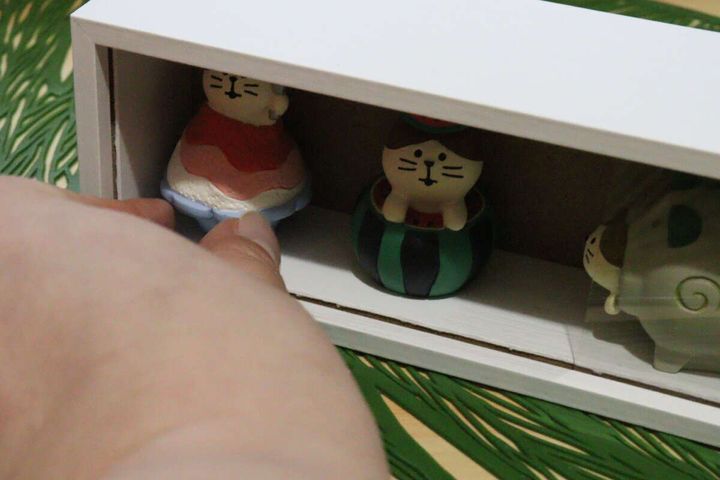 ディスプレイボックスの中に猫のマスコットを置いている手元