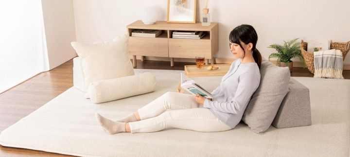 女性がグレーのソファクッションにもたれ本を読む。白いクッションも見える。