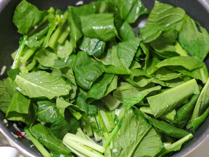 フライパンに小松菜の葉の部分も加え炒め合わせている