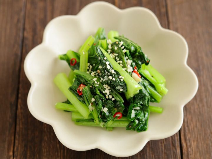 白い花形の皿に白ごまがトッピングされた小松菜のペペロンチーノ風炒め