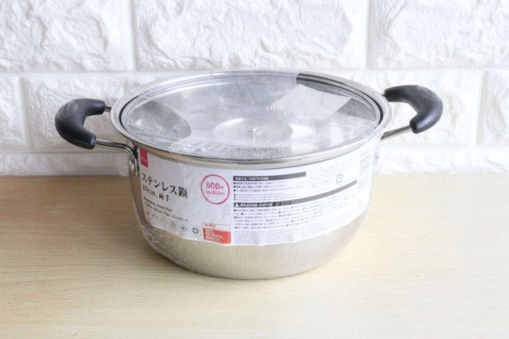 ダイソーのステンレス鍋がビニールに包まれた状態で木製のテーブルに置かれている