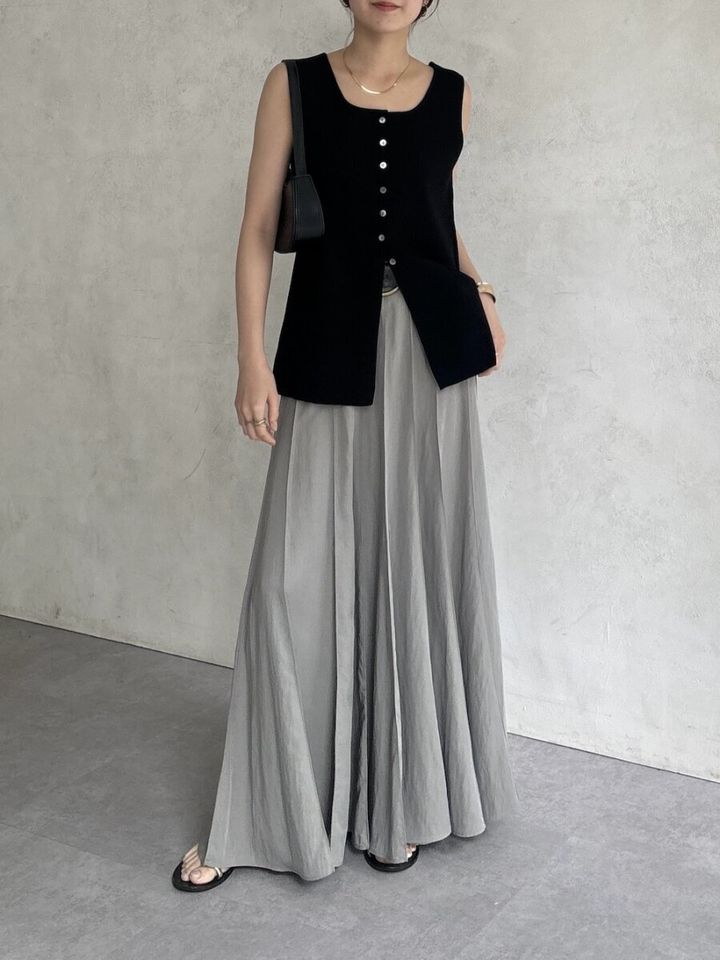 黒のボタン付きニットタンクとグレーのプリーツスカートを着用した女性