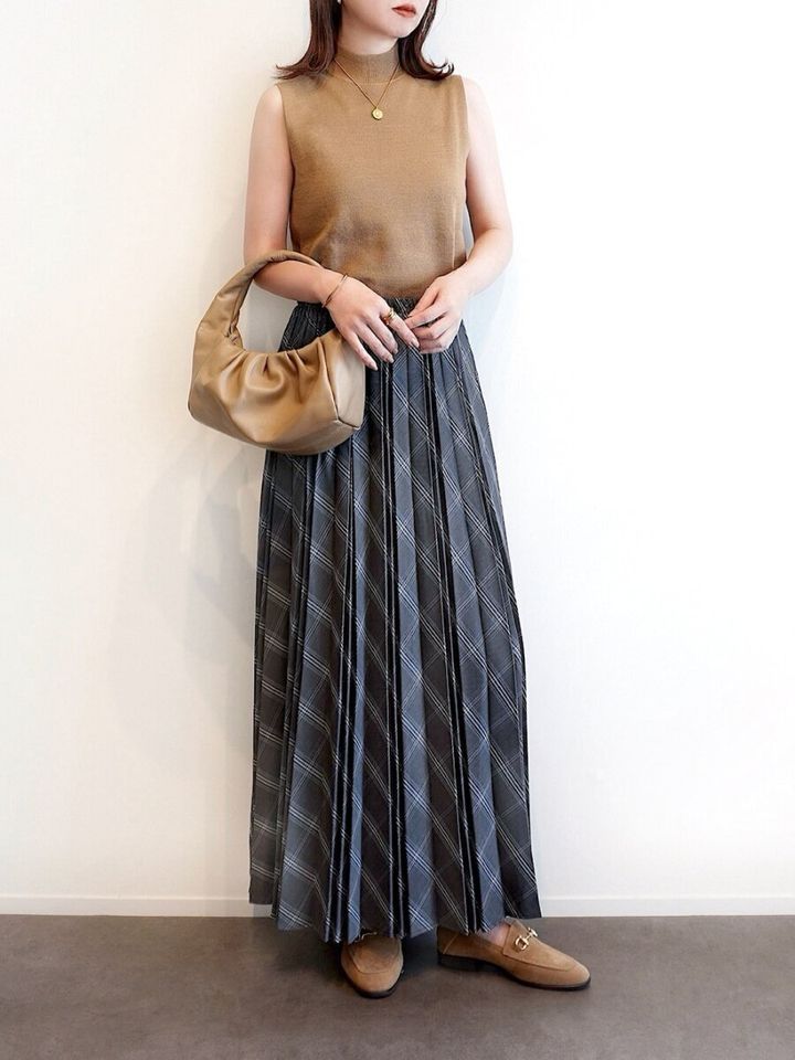 ベージュのノースリーブとグレーチェック柄プリーツスカートの女性