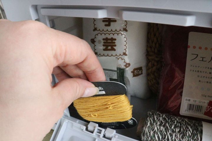 コンテナボックスの正面窓から黄色い刺繍糸を取り出している手