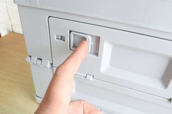 指がコンテナボックスの正面窓のロック部分を押している