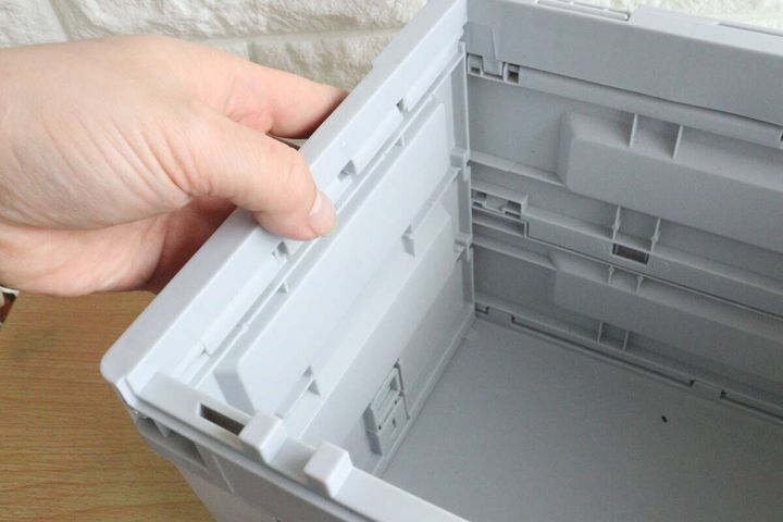 手がコンテナボックスの側面を内側から押し上げて組み立てている様子