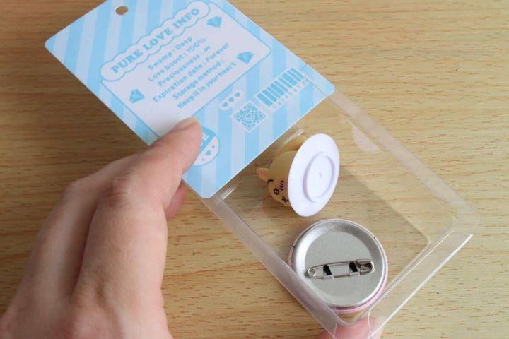 女性がブリスターパックにマスコットと缶バッジを入れる様子