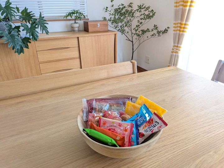 木製のテーブルの上に置かれた木製のボウル。中には個包装された様々なお菓子が入っている