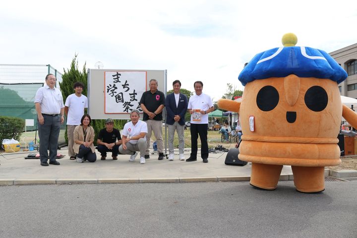 「まちまる学園祭る」看板前に集うマスコットと関係者