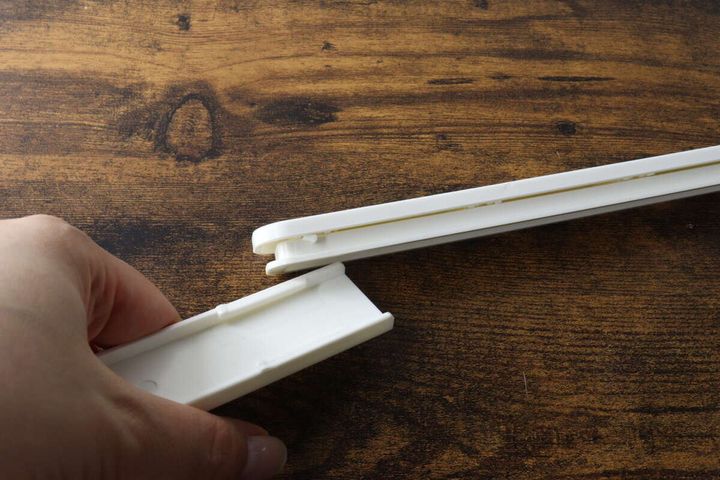 白い粘着スライド式5連収納フックを、手で分解して左右の向きを変えている様子