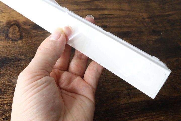 女性の手が白い粘着スライド式5連収納フックの裏面にある粘着シートを剥がしている様子