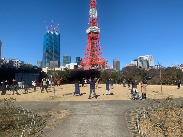 東京タワーを背景に芝生広場で体を動かす大勢の人々