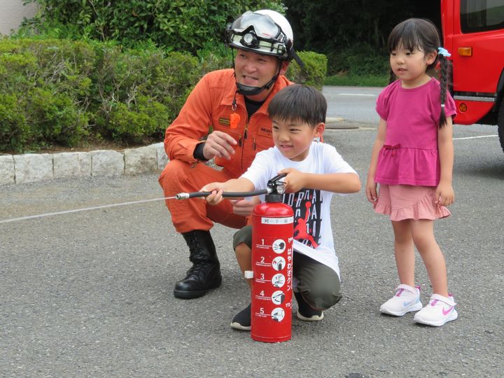 消火器体験会で消防隊員と子どもが水消火器を構える様子
