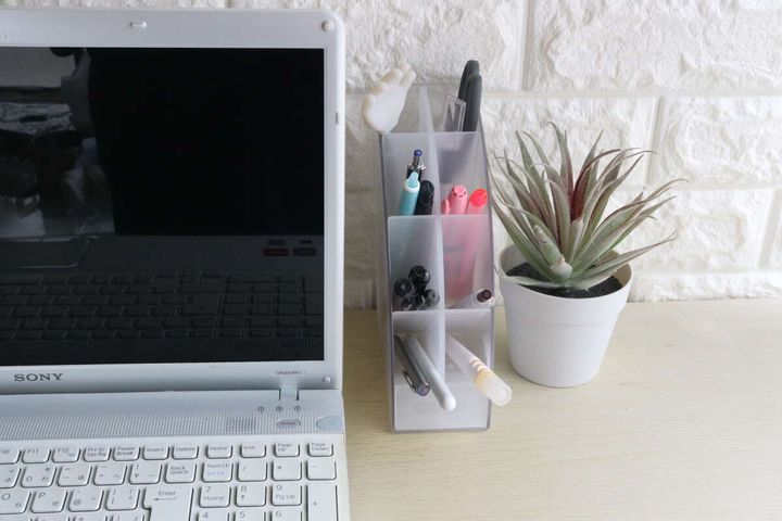デスクに置かれたノートパソコンの横に文具収納スタンドと観葉植物