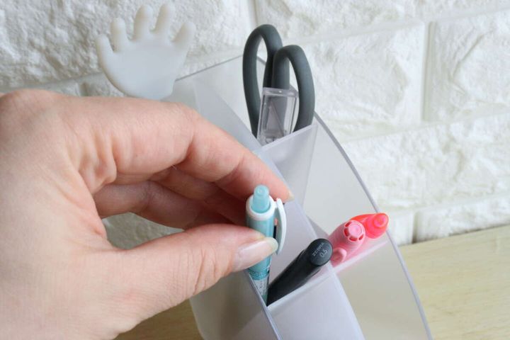 女性の指が文具収納スタンドから水色のペンを取り出そうとしている