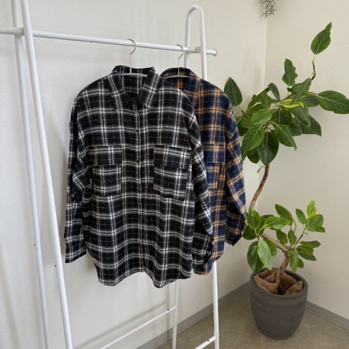 黒と青のチェック柄シャツがハンガーに並び、観葉植物が背景にある