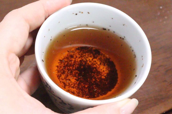 抽出後の紅茶が入ったカップを女性の指が持っており、細かい茶葉が底に沈んでいる