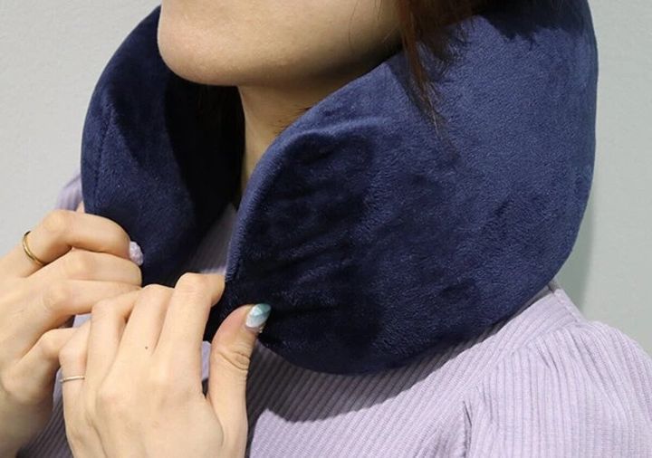 女性が紺色のネックピローを首に装着しボタンを留めている