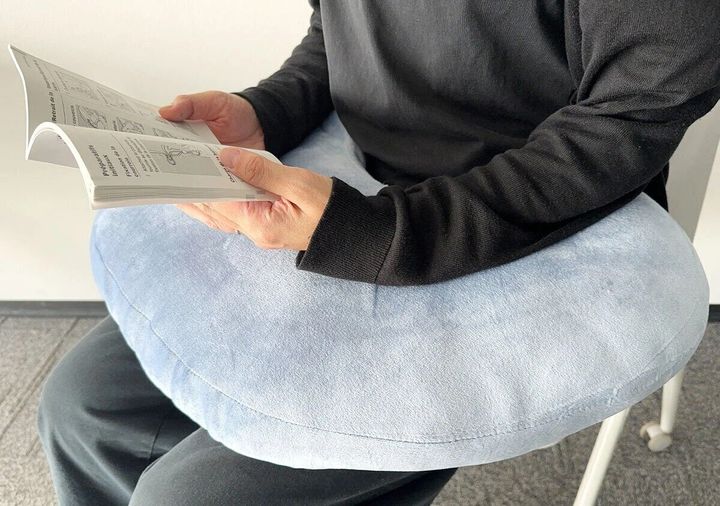 男性が青いもちもちクッションを腰に当てて本を読んでいる