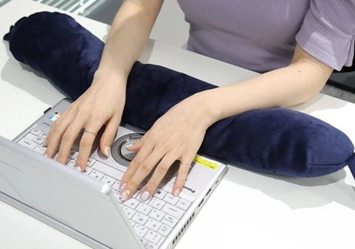 女性が紺色のネックピローをアームレストとしてPC作業している