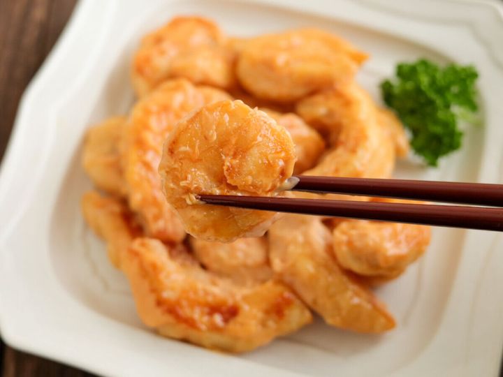 箸で持ち上げられた、マヨソースが絡んだ鶏マヨのクローズアップ