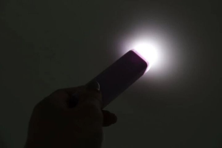 暗闇で紫色の防犯ブザーの先端から白いライトが光る様子