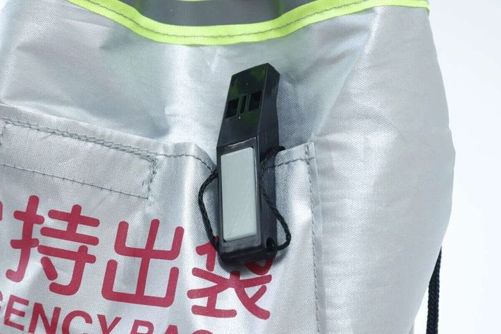 銀色のリュックのポケットに黒いホイッスルがクリップで留められている