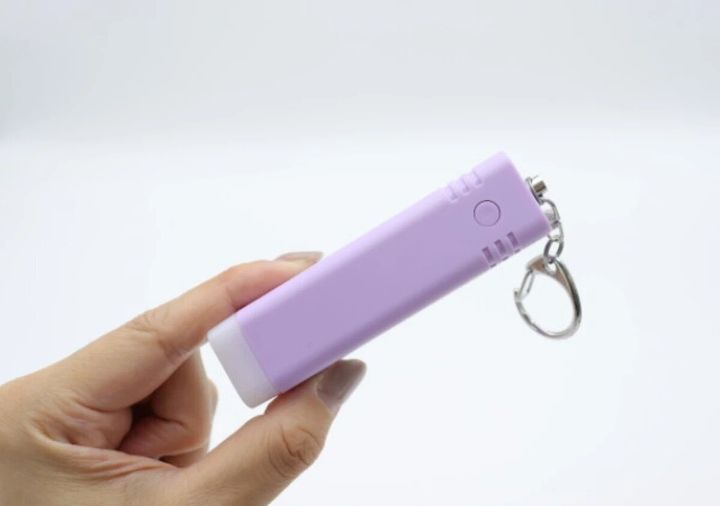 女性が紫色の防犯ブザーを指で挟んで持っている手元
